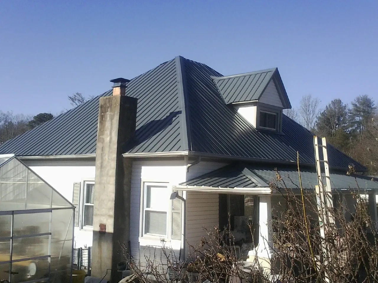 Dark blue standing seam metal roof on a white farmhouse with dormer — Slate & Tile Roof Repair by Roofing Brothers in Alden