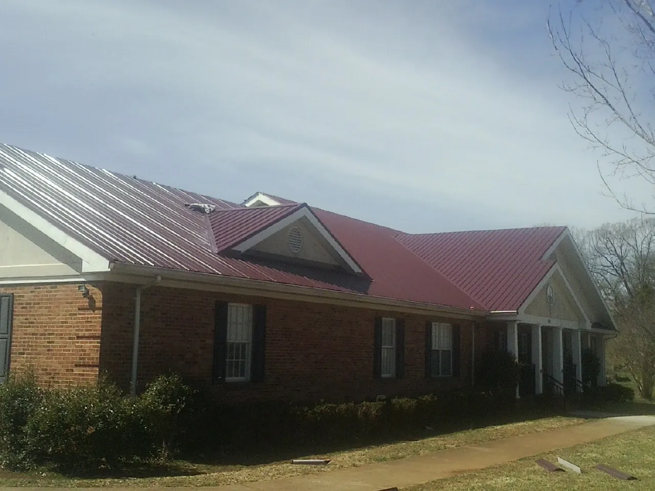 Red metal roof with gabled entries on a long brick building, from a Hail Damage Roof Repair job in Alden