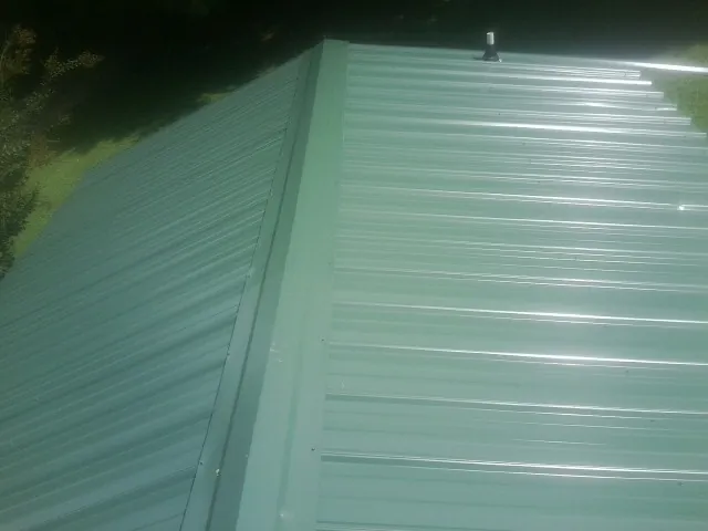 New green metal panels meeting at the ridge of a roof — Flat Roof Repair work by our crew in Alden